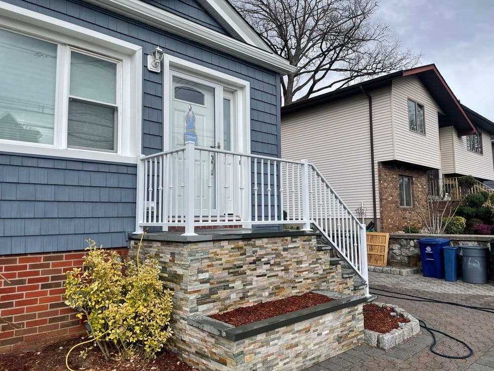 House entrance with stone steps, white railing, and landscaped garden. Modern home exterior.