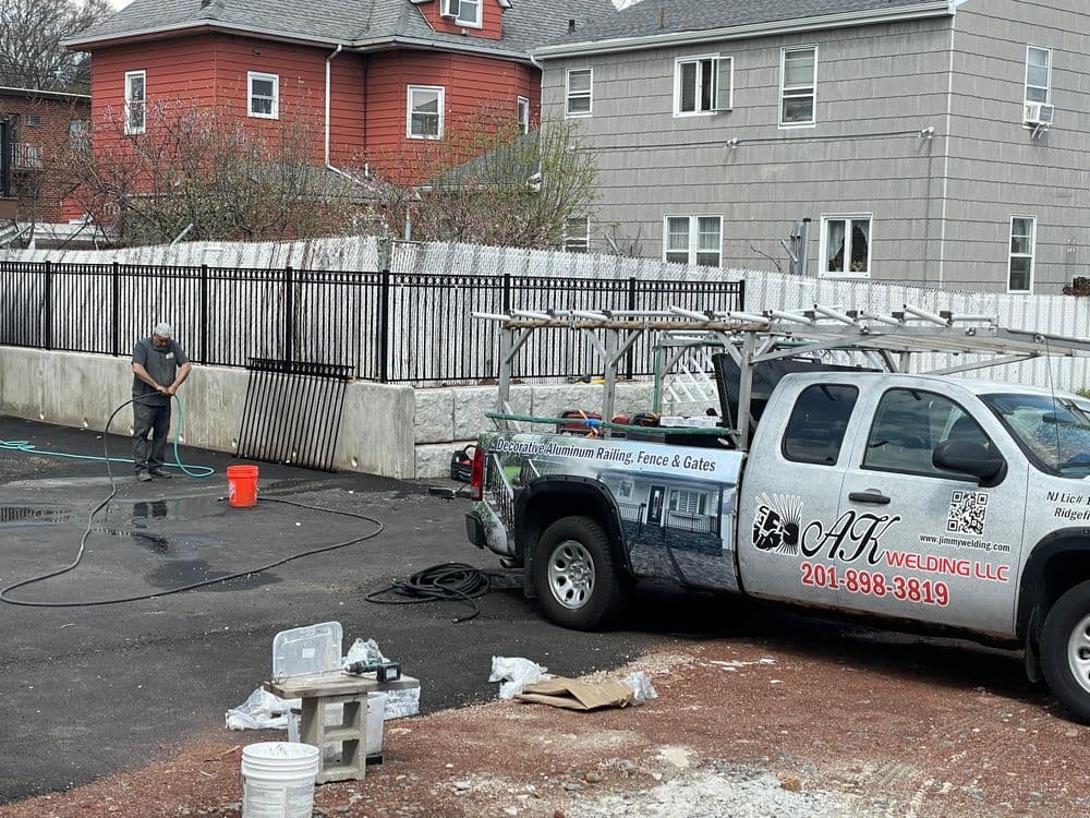 Man cleaning tools near a pickup truck marked AK Welding LLC, surrounded by construction materials.