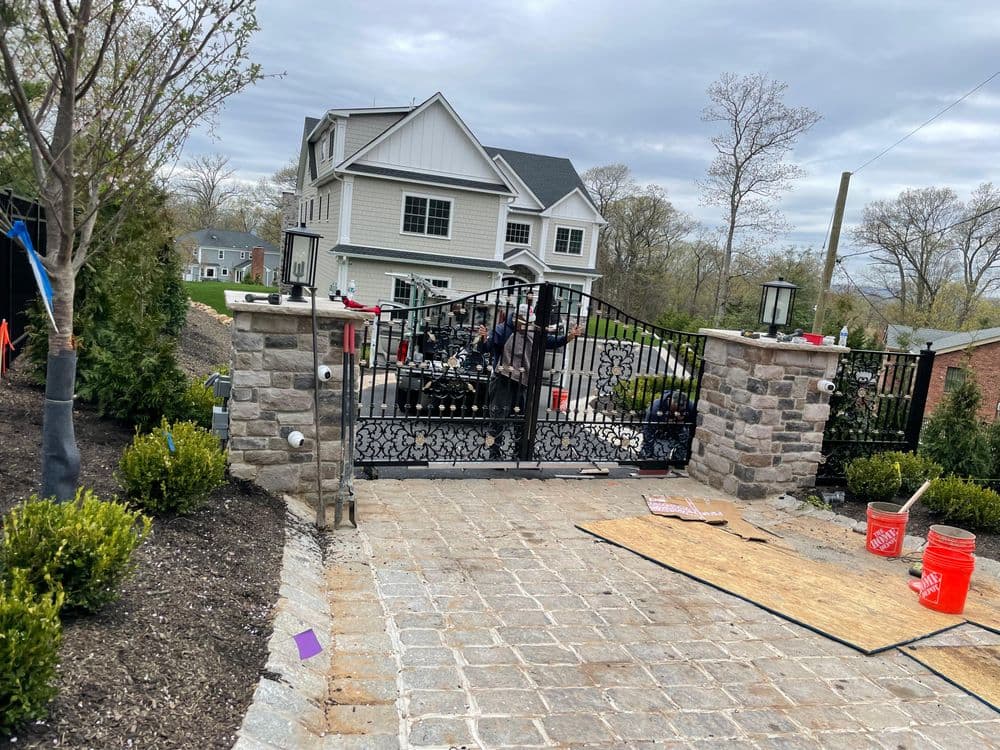 Residential property with a stone driveway, black iron gate, and home renovation in progress.