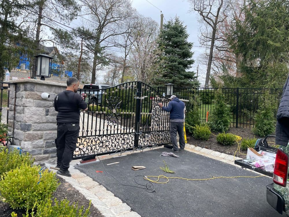 Two workers installing a decorative black metal gate at a residential property entrance.