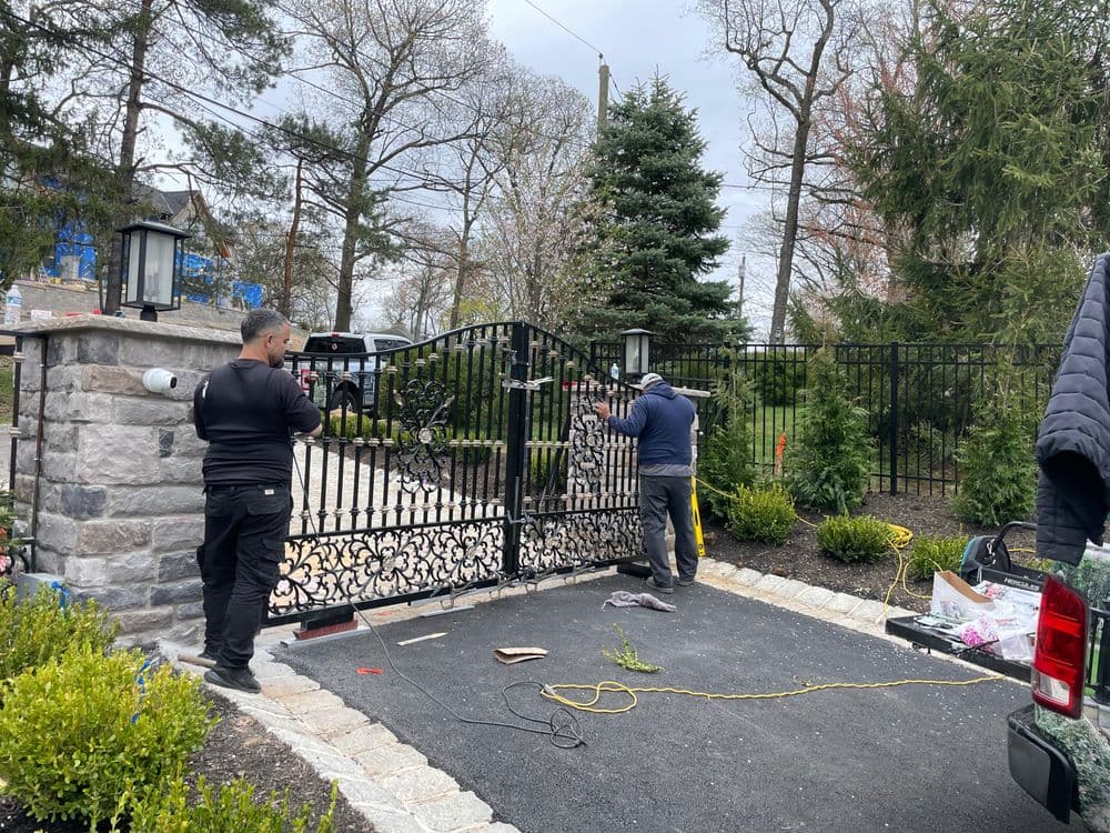 Two workers installing a decorative metal gate in a landscaped entryway.