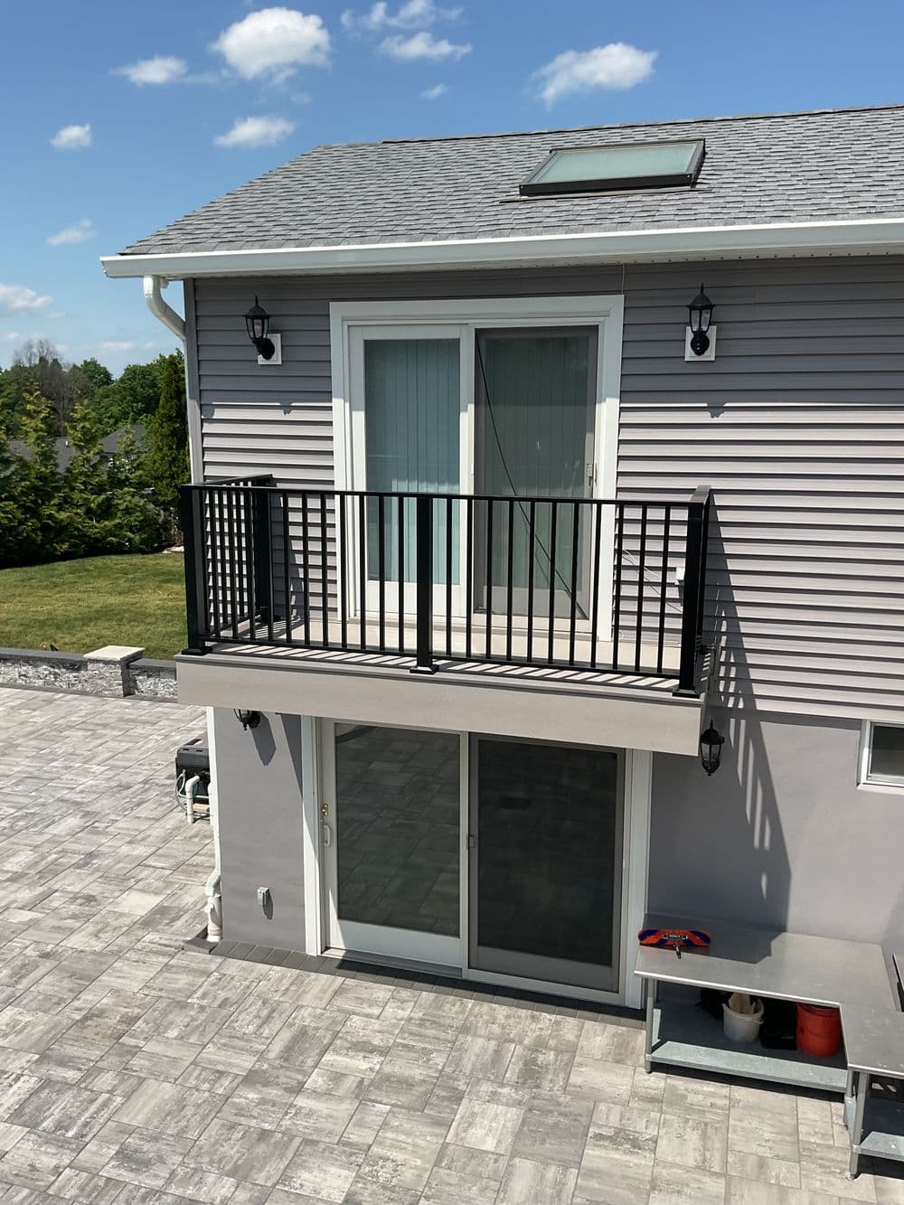 Contemporary home exterior featuring a balcony, stone patio, and clear blue sky.