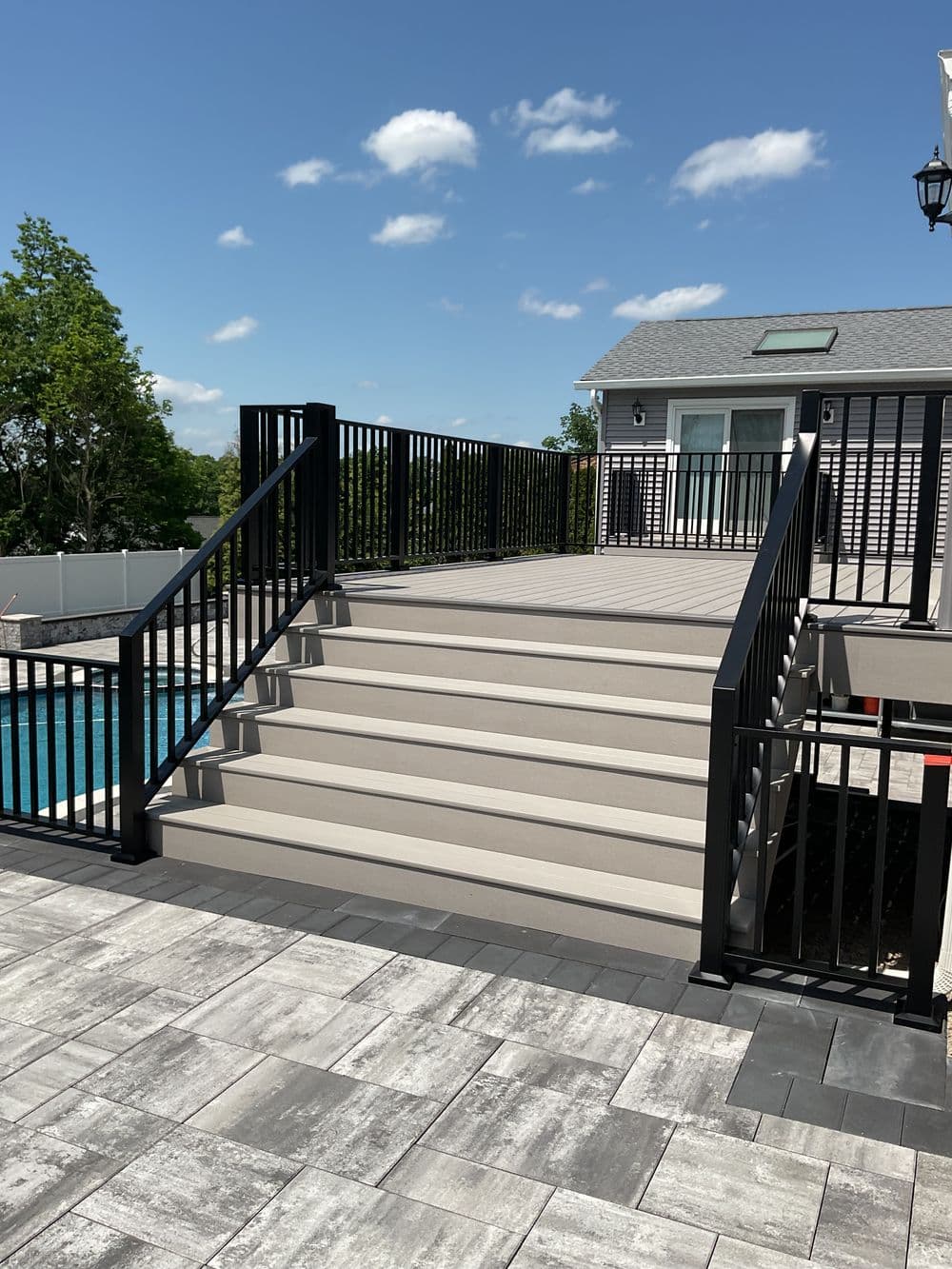 Modern outdoor staircase with black railings leading to a pool area on a sunny day.