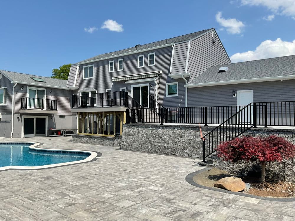 Modern home with poolside patio, landscaped yard, and spacious deck under a blue sky.