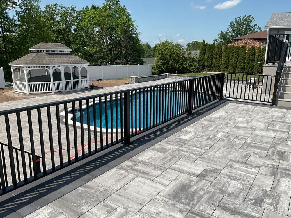 Modern patio with black railing overlooking a blue pool and gazebo in a suburban backyard.
