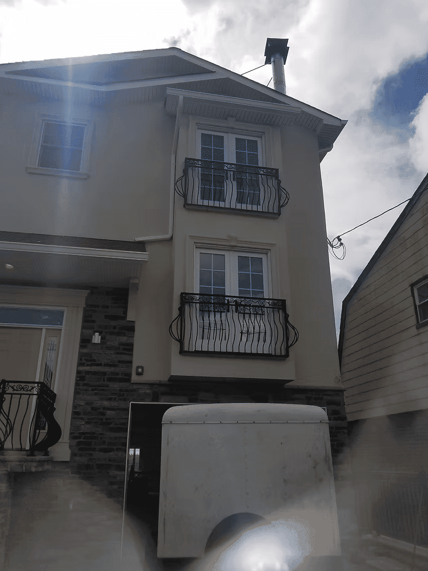 Two-story residential home with decorative balconies and a white utility trailer in front.