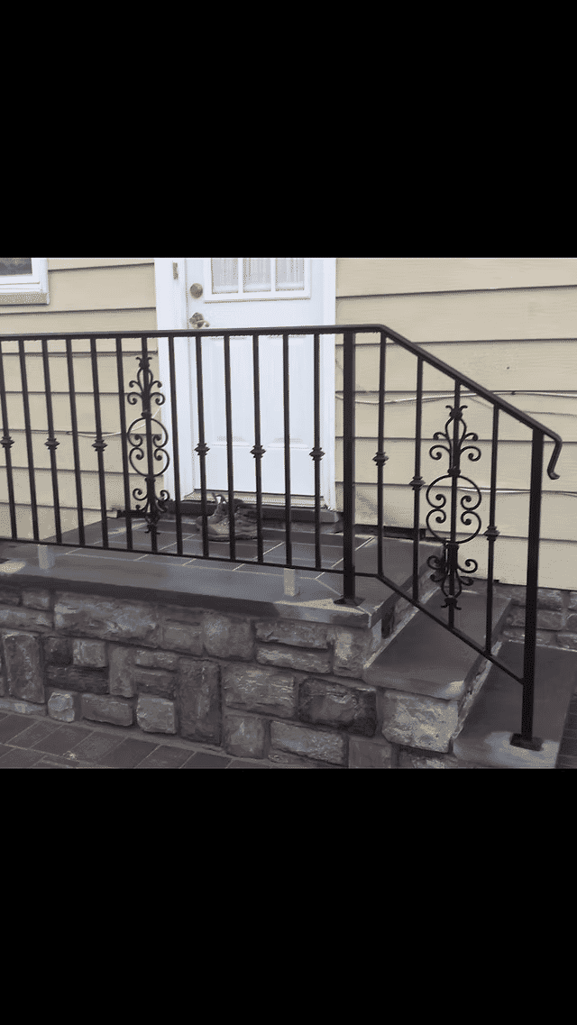 Black wrought iron railing on a stone step leading to a white door. Elegant design details visible.