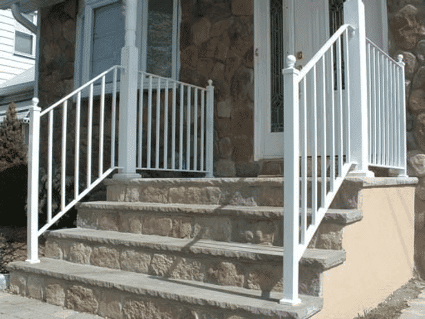 White railing on stone steps leading to a front door of a home with a stone facade.