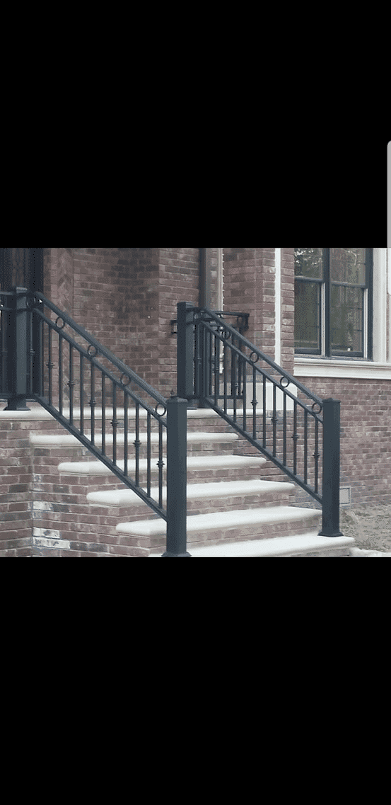 Black metal railing on brick staircase leading to a modern entrance with large windows.