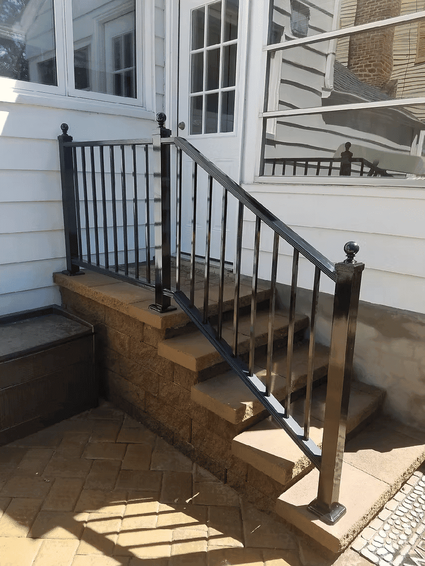 Black metal railing leading up a stone staircase to a white house exterior.
