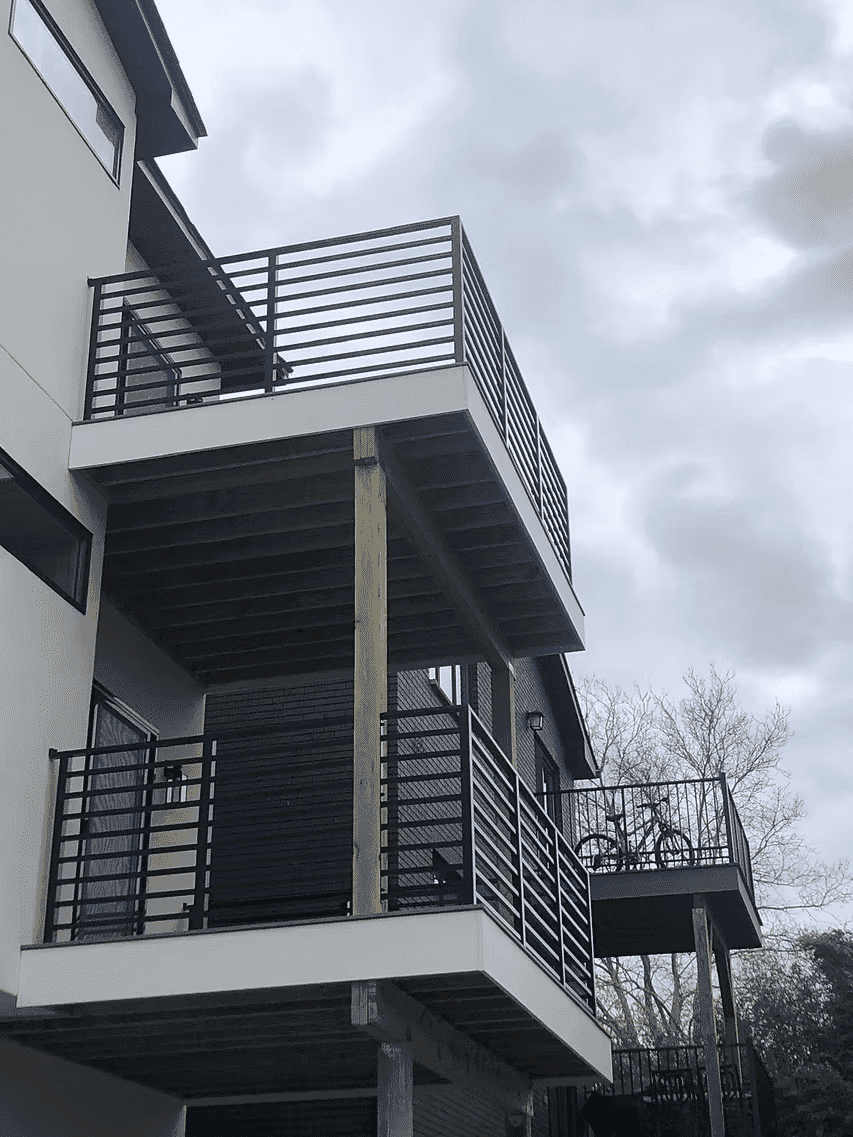 Modern two-story building with two balconies featuring black railings against a cloudy sky.