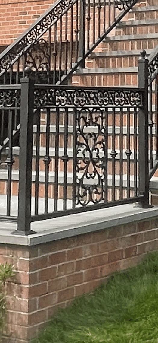 Wrought iron railing with decorative patterns near brick staircase and green lawn.