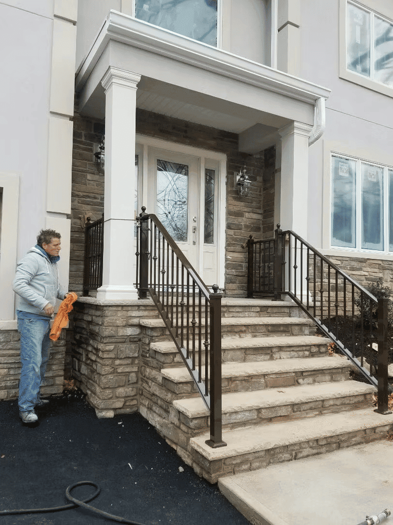 Man cleaning stone steps and railings in front of a modern house entrance.