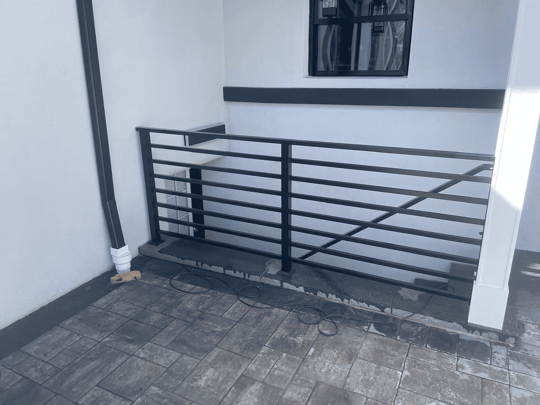 Black metal railing on a modern exterior staircase with stone flooring and white walls.