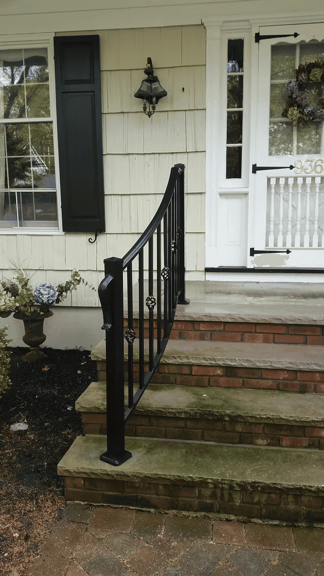 Black metal handrail on steps leading to a front porch with decorative flowers and a lantern.