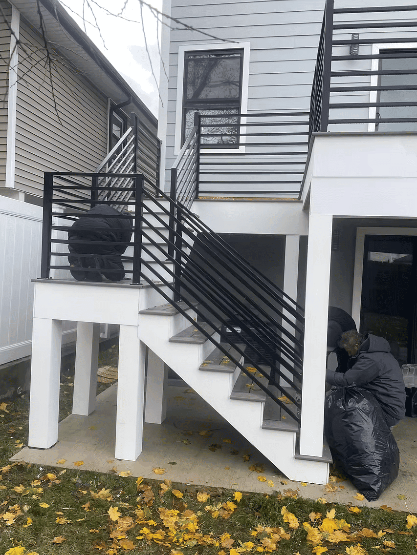 Workers installing modern black railings on an outdoor staircase near a house.