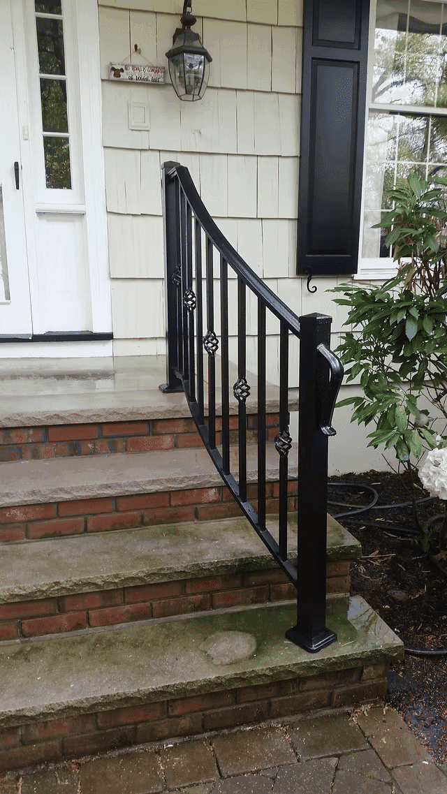 Black metal railing on brick steps leading to a house entrance with a lantern.