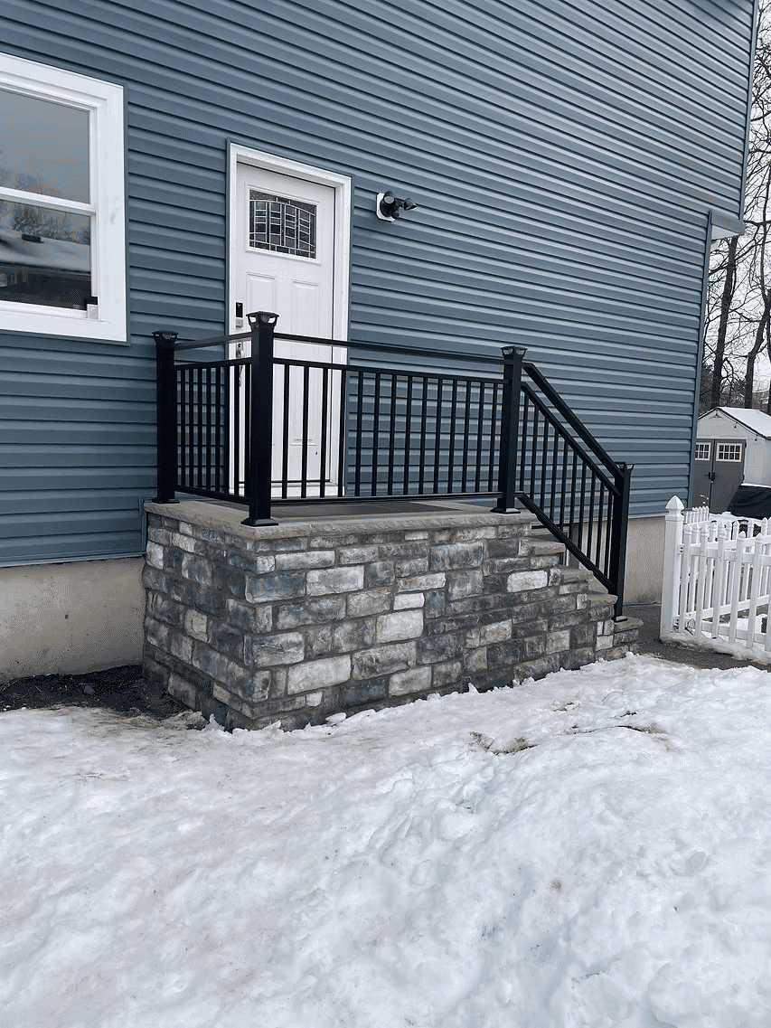 Modern stone steps and black railing leading to a white door on a blue house exterior.