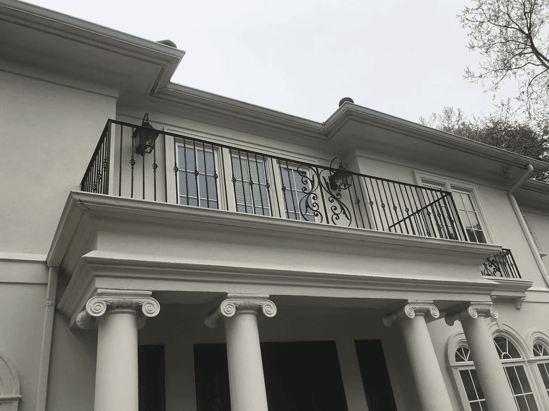Elegant white house exterior with a balcony featuring decorative iron railing and classic columns.