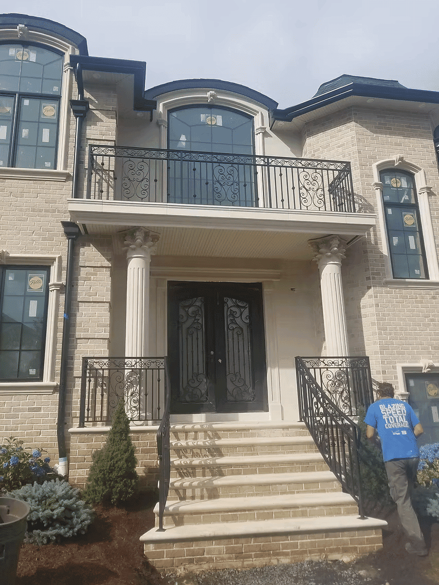 Elegant new home entrance with wrought iron railings, columns, and large double doors.