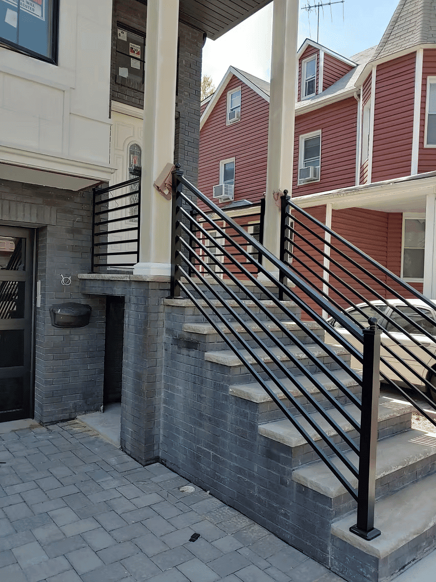 Modern black railing on stairs leading to a residential building with brick facade.