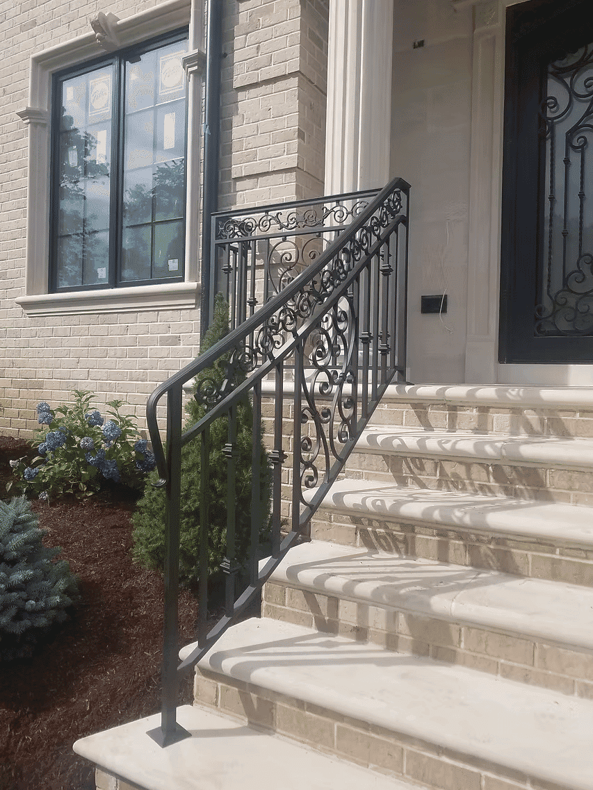 Wrought iron railing on elegant staircase leading to a modern brick house entrance.