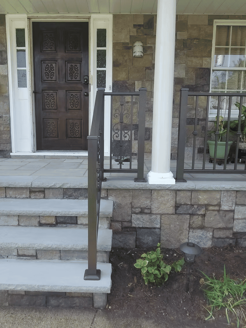 Front porch with stone steps, handrail, potted plants, and a decorative wooden door.