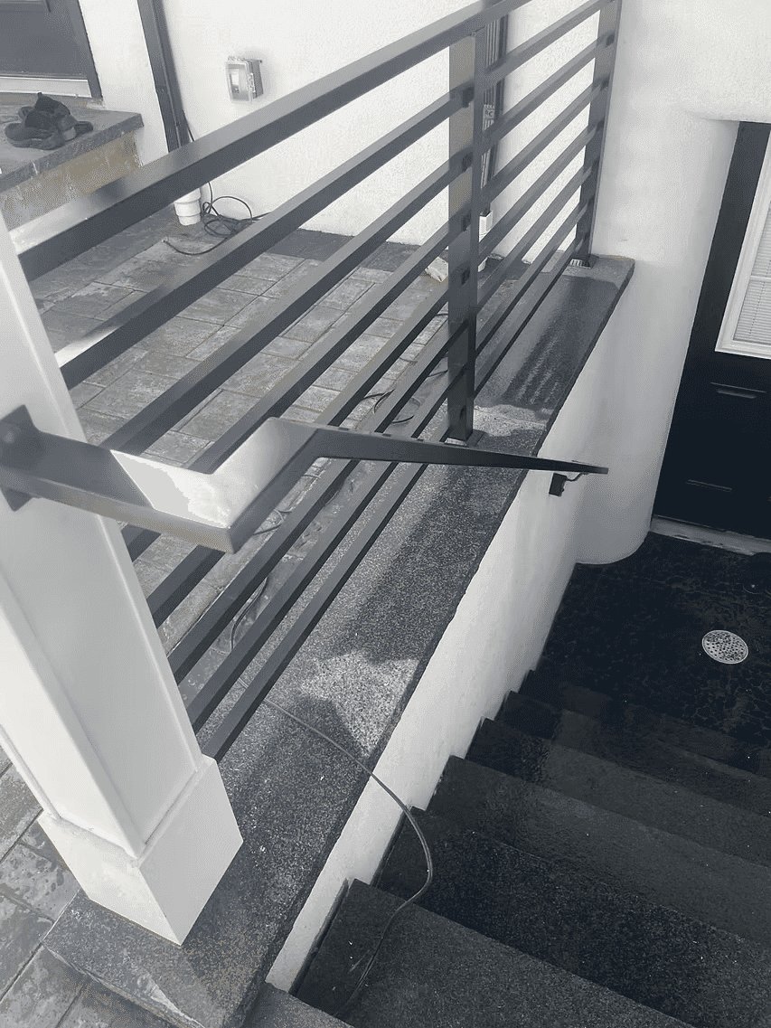 Modern black railing on granite steps leading to a entrance, with visible cable and surface details.