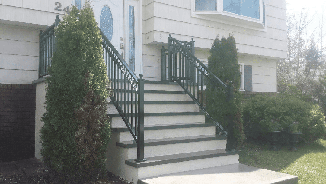 Metal railing staircase leading to a residential entrance, surrounded by shrubs and landscaping.