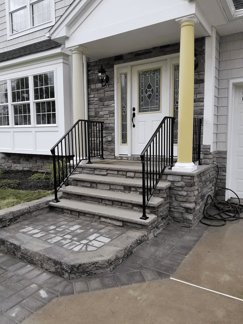 Front porch with stone steps, black railings, and decorative glass doors in a suburban home.
