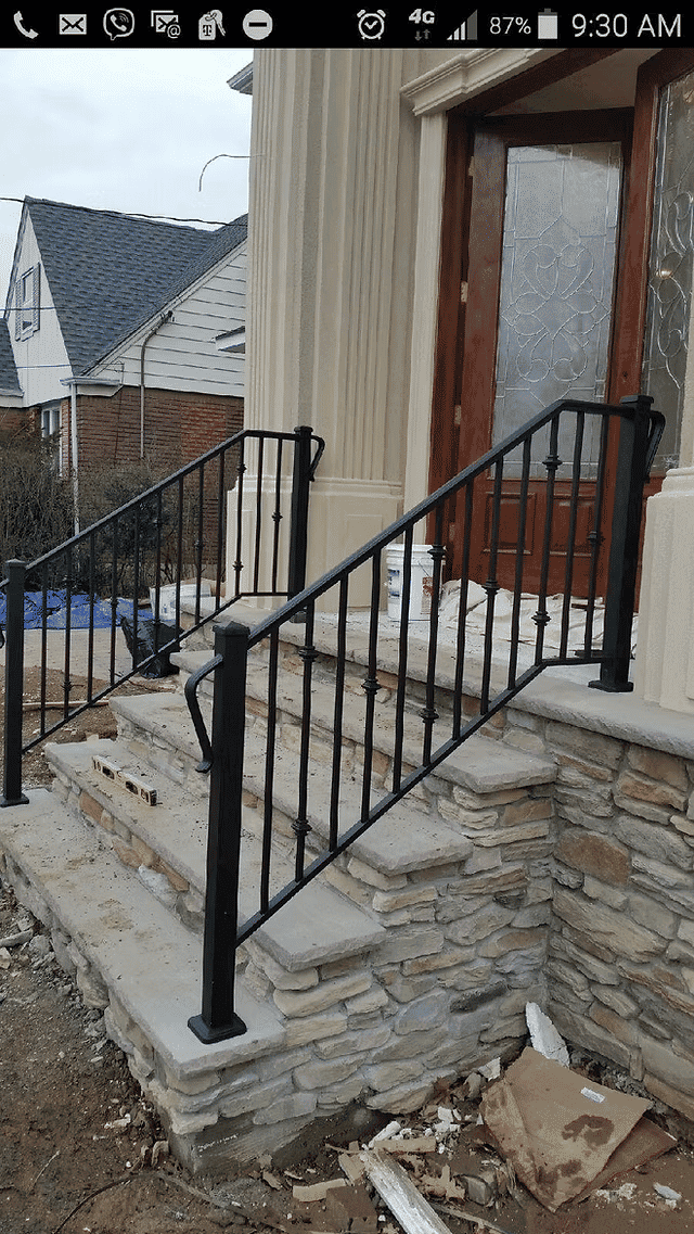 Black metal railing on stone stairs leading to a wooden front door in a residential area.