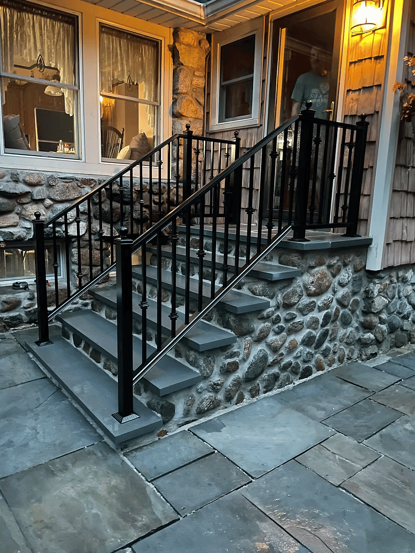 Black metal railing on stone steps leading to a home's entrance, with outdoor lighting.