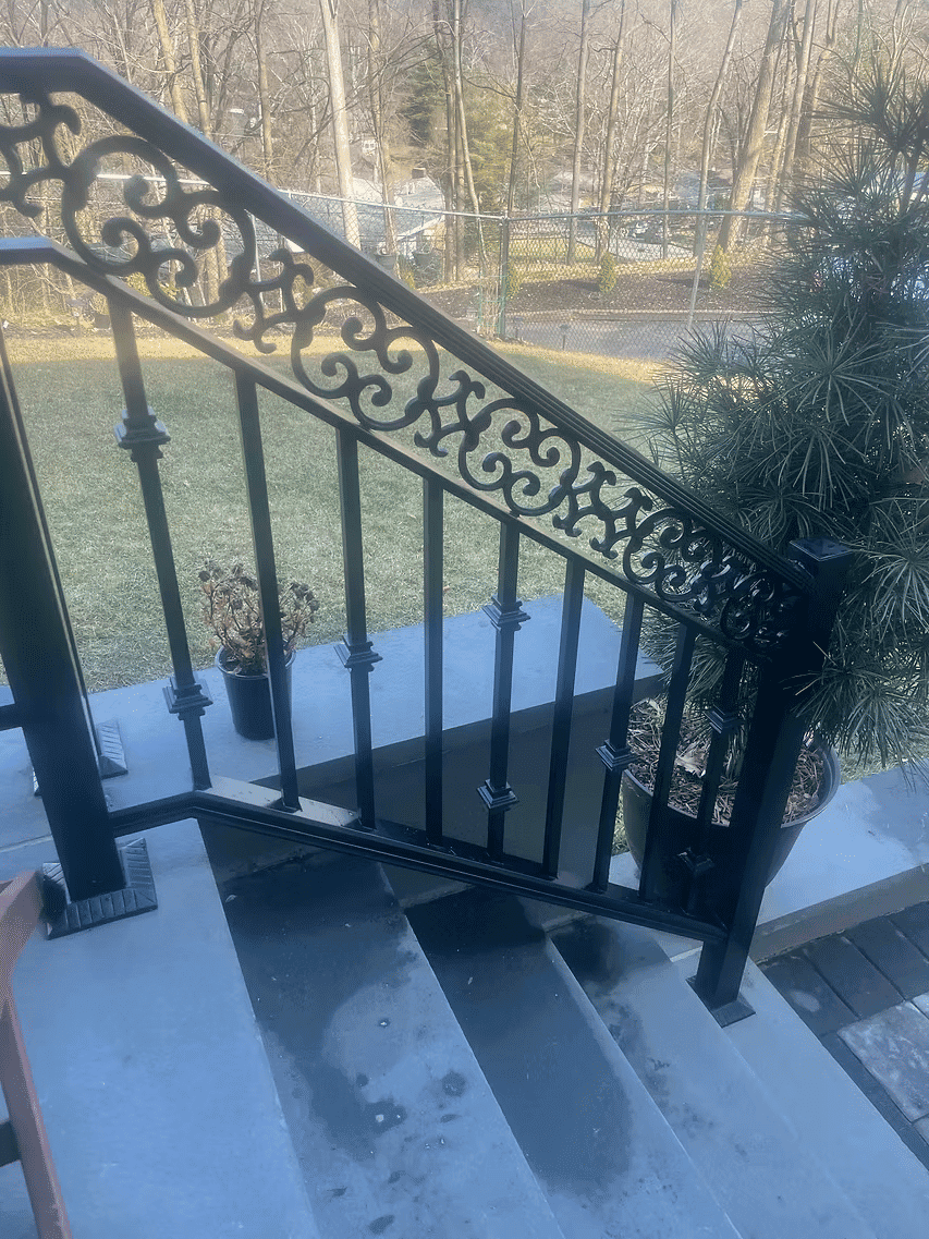 Black wrought iron railing on stone steps with a planter and green lawn in the background.