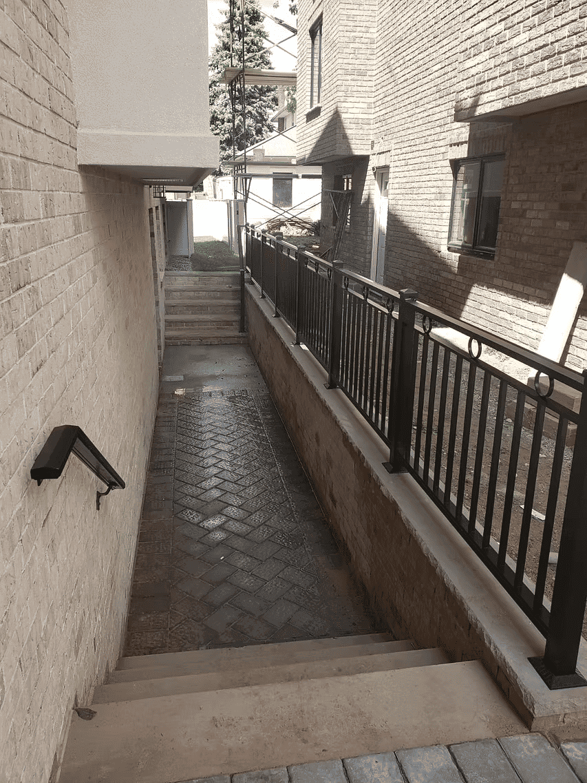 Narrow outdoor stairway between brick buildings with decorative fencing and sunlight.