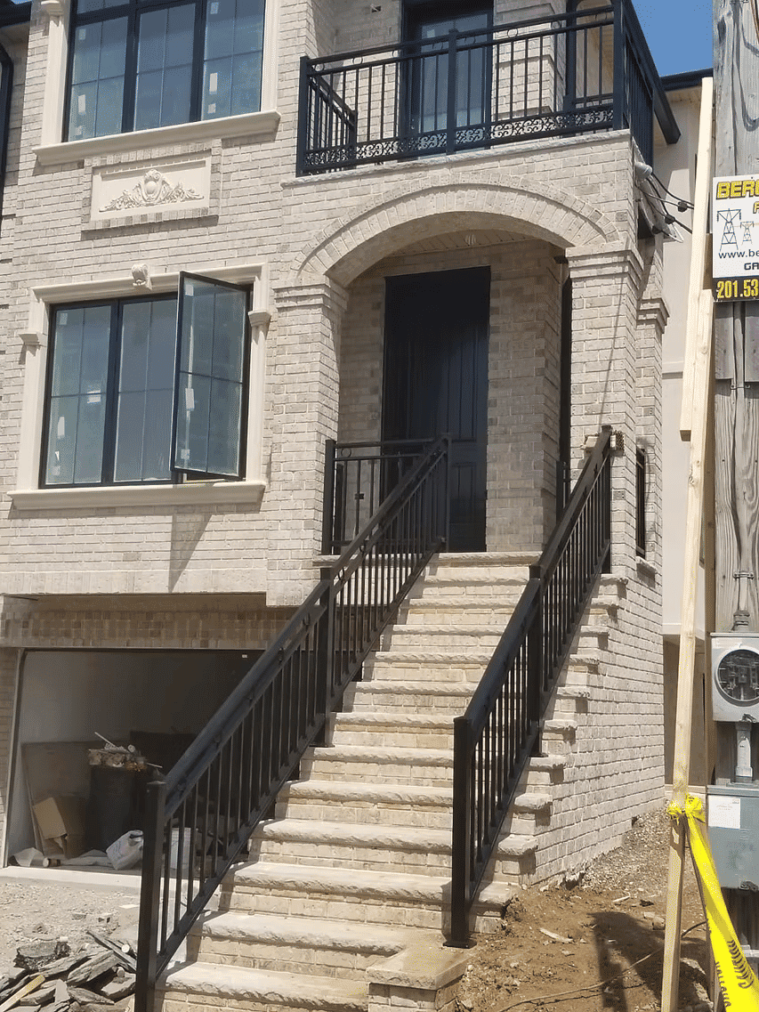 Newly constructed home with stone facade, front door, and staircase. Construction site details visible.