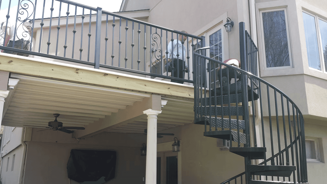 Spiral staircase leading to a second-story deck with railings and outdoor furniture.