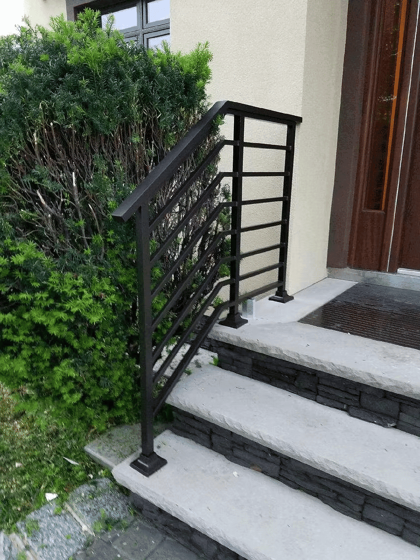 Metal railing on outdoor steps next to a bush, leading to a front door.