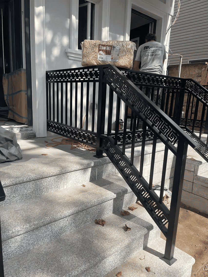 Black metal railing and steps leading to a house under construction, with a worker nearby.