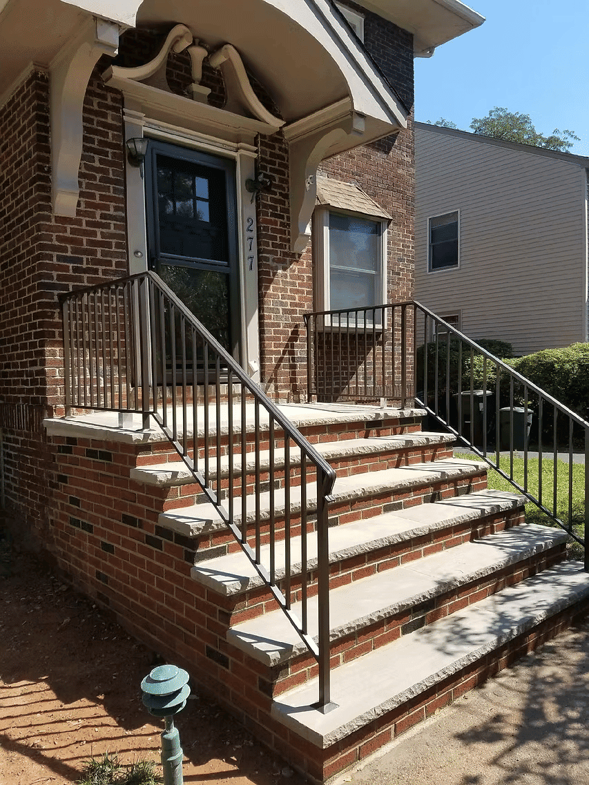 Brick house entrance with wide steps and metal railing at 277, featuring lush green surroundings.