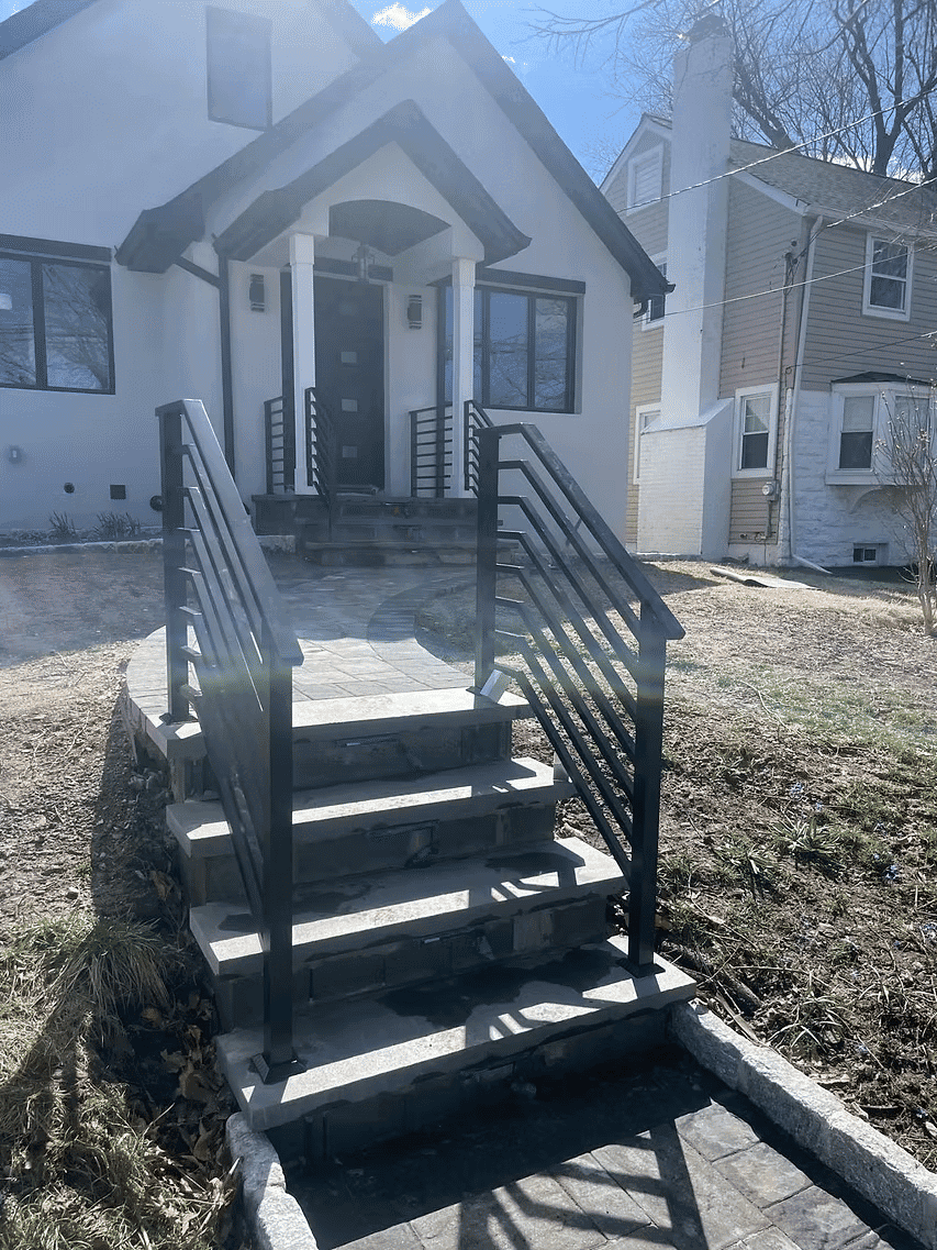 Modern home entrance with stylish stone steps and black railing in sunny setting.
