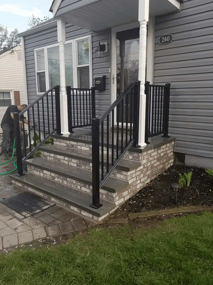 Black metal railings on a concrete porch with stone steps and landscaping at a residential home.