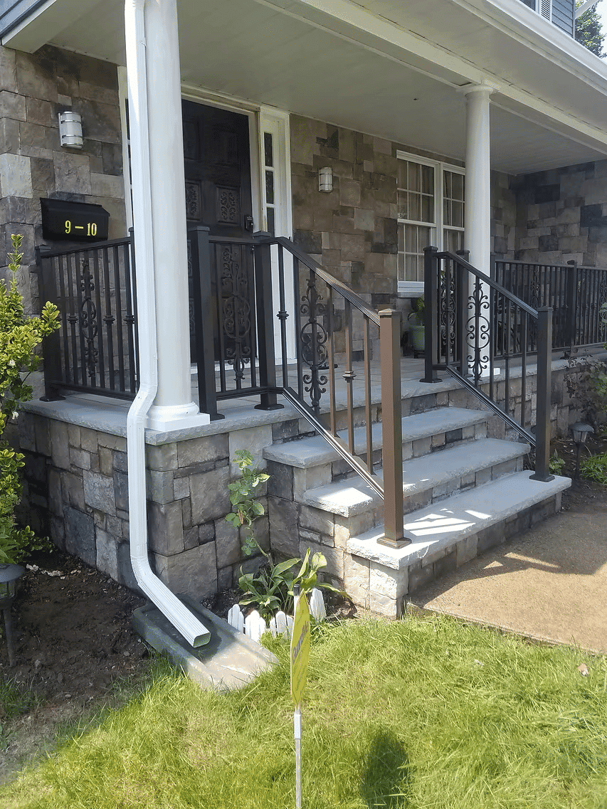 Front entrance of a stone house with stairs, railings, and landscaping details.