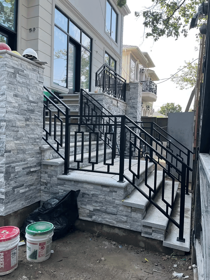 Modern stone staircase with black metal railing beside residential buildings.