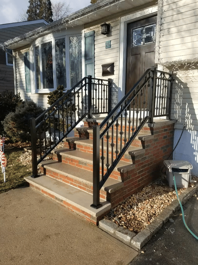 Black wrought iron railing on brick steps leading to a home entrance, decorated for the holidays.