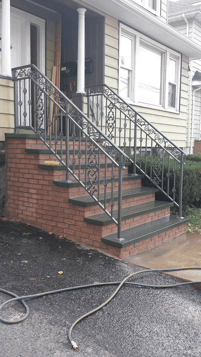 Wrought iron railing on brick steps leading to a home entrance with landscaping.