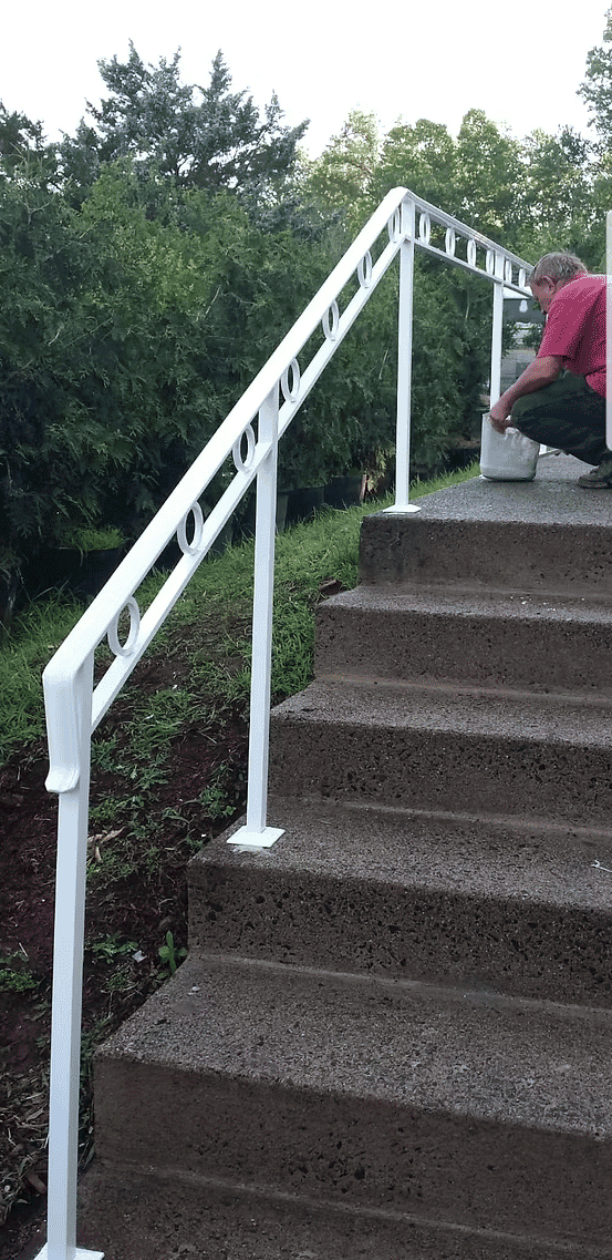 White metal railing installed on concrete stairs, with a person working near the bottom.