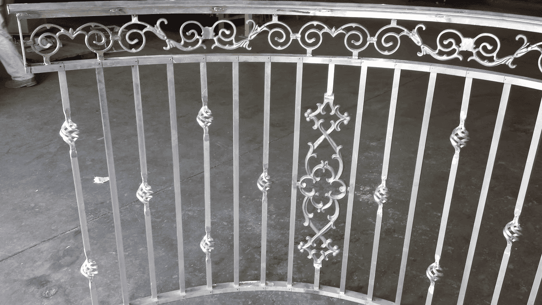 Intricately designed metal railing with decorative patterns and vertical bars on a concrete floor.
