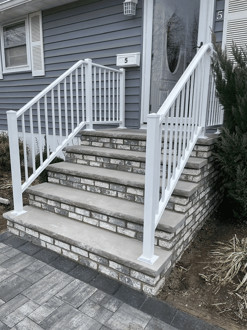 White railing on brick steps leading to a gray house entrance with a door.
