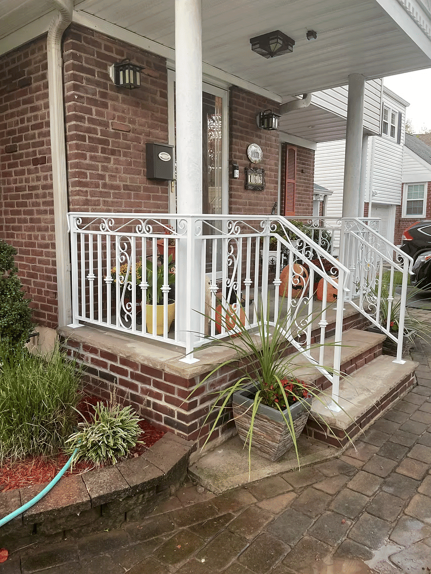 White wrought iron railing on brick porch steps adorned with potted plants and landscaping.
