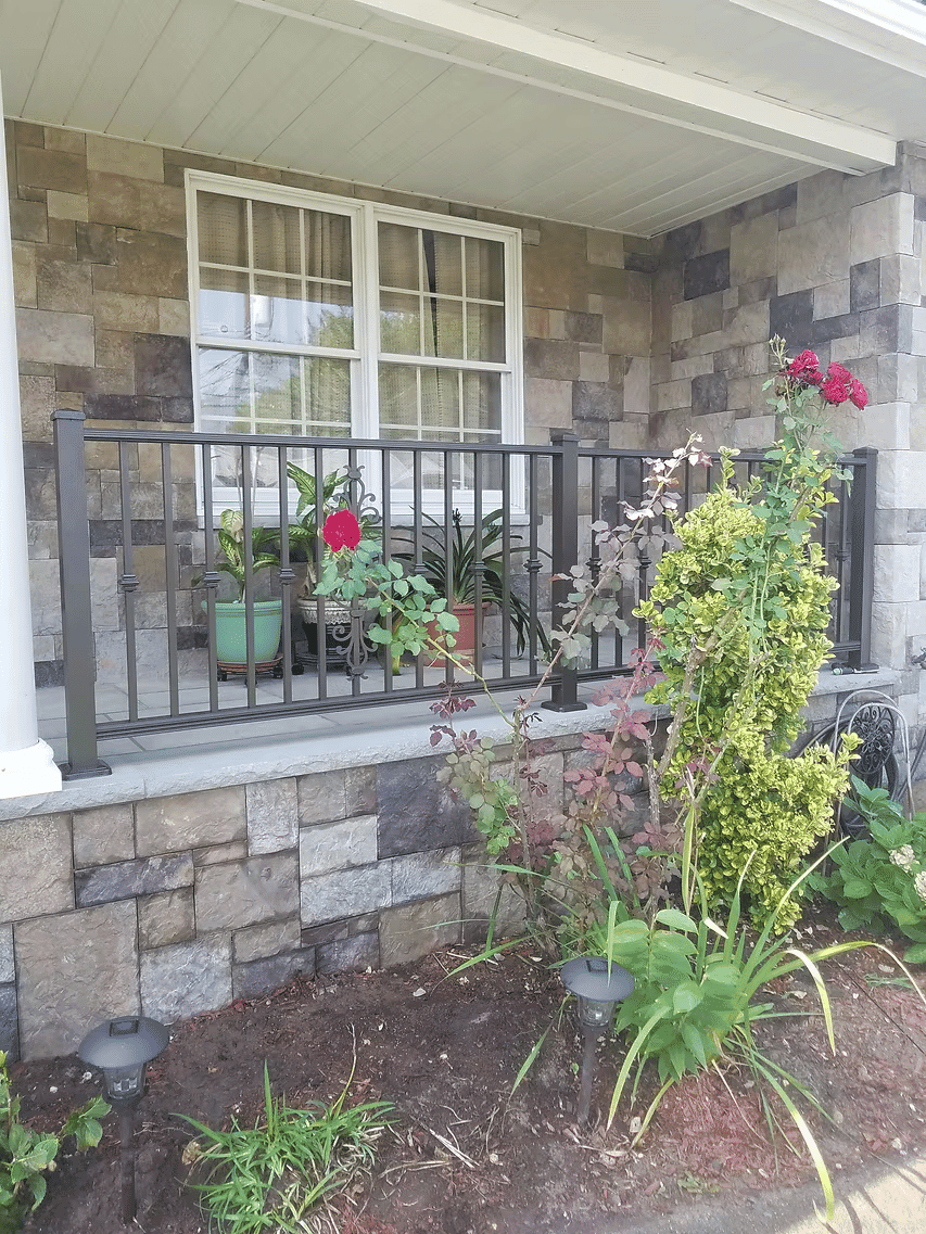 Front porch with stone walls, potted plants, and vibrant flowers adding color and charm.